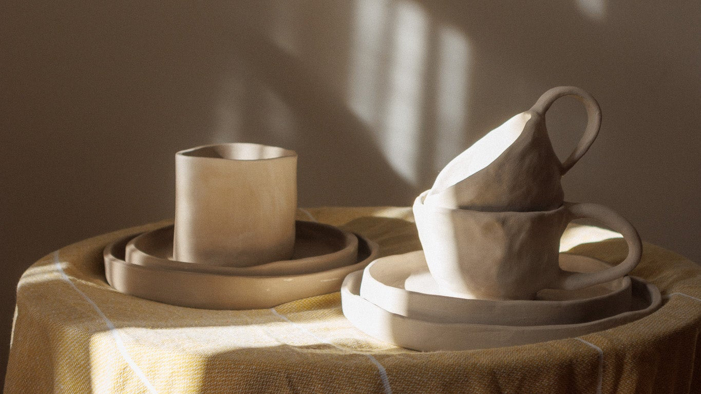 Set of ceramic cups and bowls on a textured surface with soft lighting